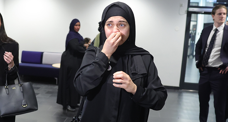 Hon är i korridoren utanför salen för rättegången. Hon gråter. Hon torkar sig med ett papper i ansiktet.