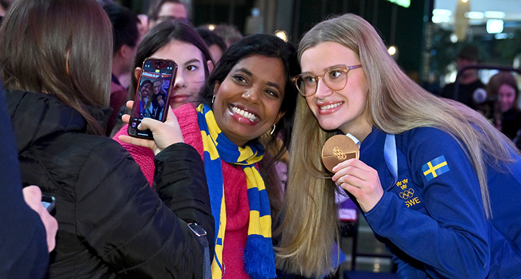 Hon visar sin medalj och ler mot en person som tar en bild med mobil.