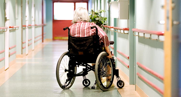 En korridor på ett hem för gamla. En bit bort sitter en kvinna i en rullstol. Vi ser henne bakifrån.