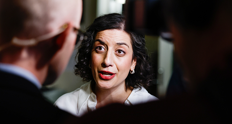 Hon står och pratar i en mikrofon. Hon pratar med journalister. Hon blir filmad också.