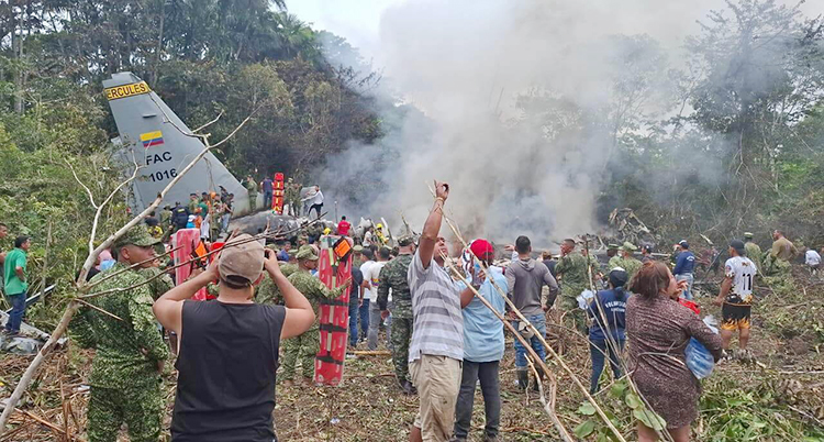 Ett flygplan har kraschat i en skog. Det kommer rök från flygplanet. Massa människor står vid planet.