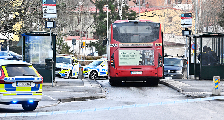 En röd buss som står stilla. Runt om står flera polisbilar.