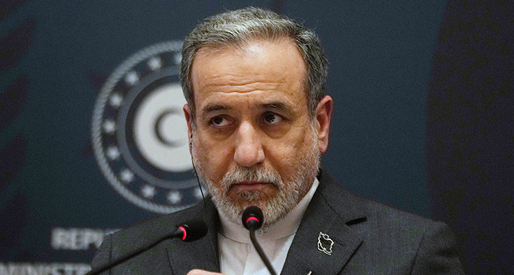 Han har skägg och en mikrofon framför sig.