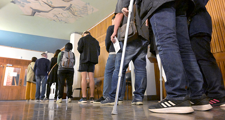 En bild från valet år 2022. Människor står i kö för att rösta. De står inne i en skola.