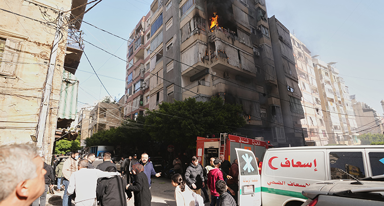 människor på en gata i en stad. Ett höghus brinner efter en träff av någon slags bomb.