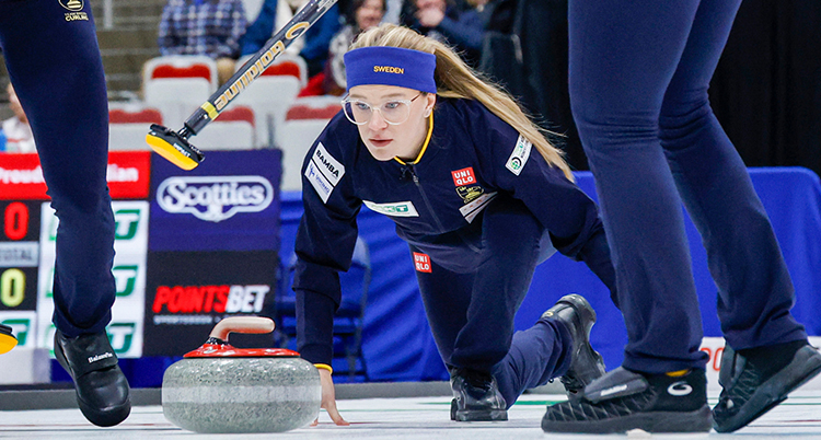Hon soitter på isen efter att ha puttat iväg en sten. Vid sidorna syns ben från andra spelare.