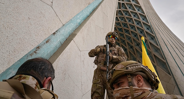 Tre soldater utanför ett hus. De har vapen och gröna kläder.