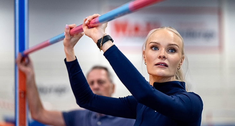 Hon står vid ribban i höjdhopp. Hon håller i ribban.