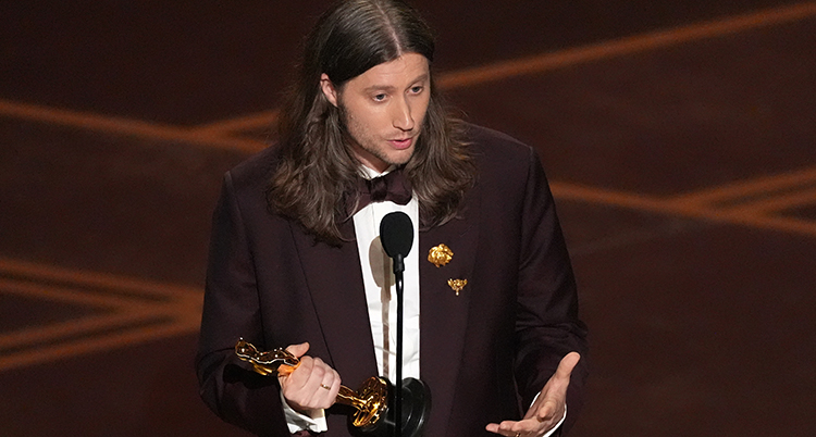 Han står på en scen och pratar i en mikrofon, Han har priset i ena handen.