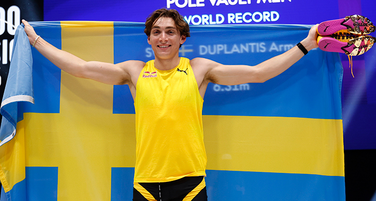 Han håller en svensk flagga bakom ryggen. Han är glad.