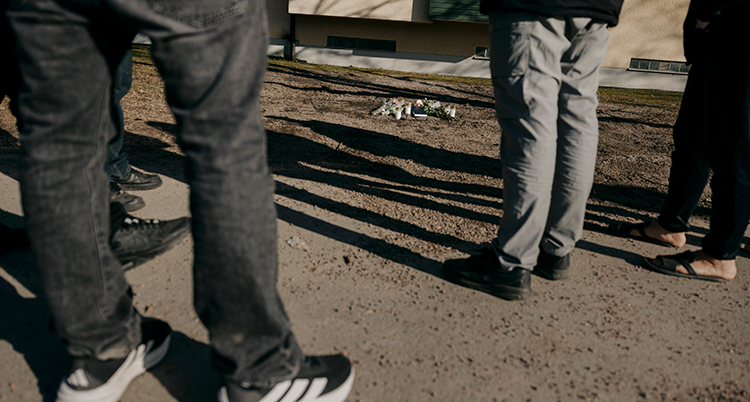 Flera människor står runt blommor och ljus på marken.