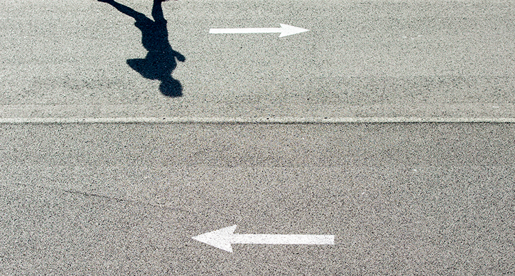 En väg med två pilar. Man ser också skuggan av en människa.