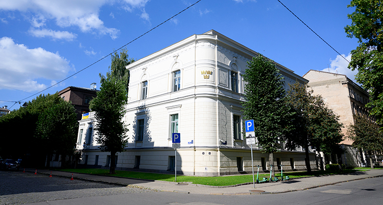 Ett vitt hus i Riga. Det är träd utanför. Himlen är blå.