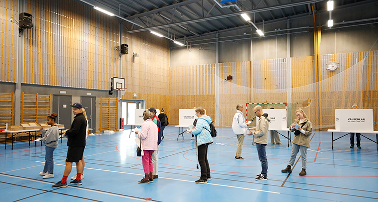 Folk står i kö inne i en gympasal. De ska rösta. Det är valet år 2022.
