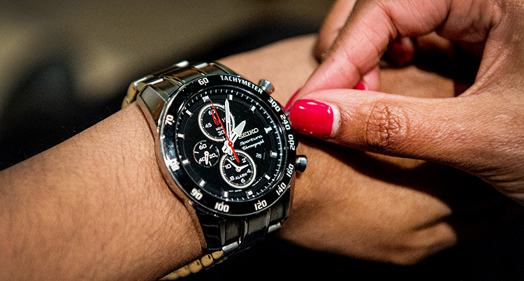 Närbild på en klocka som sitter på en arm. En hand skruvar på klockan.