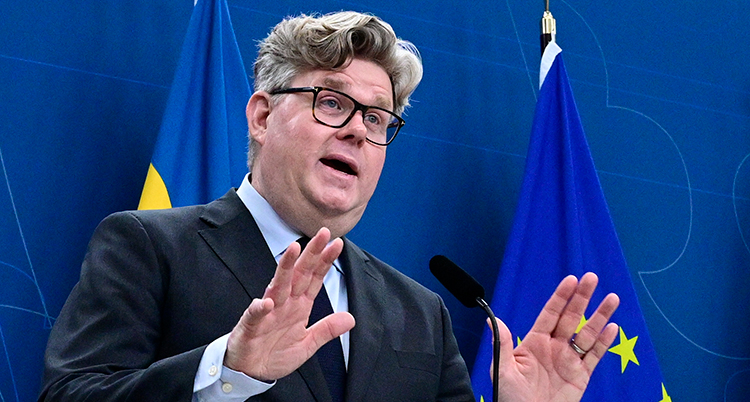 Han pratar på ett möte med journalister. Bakom syns Sveriges flagga.