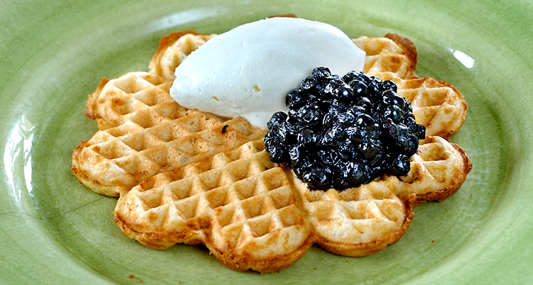 En närbild på en våffla med grädde och sylt. Våfflan ligger på en grön tallrik.