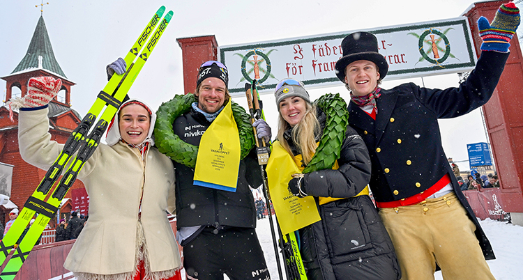 Fyra glada personer är glada och vinkar. De står framför målet i Mora.