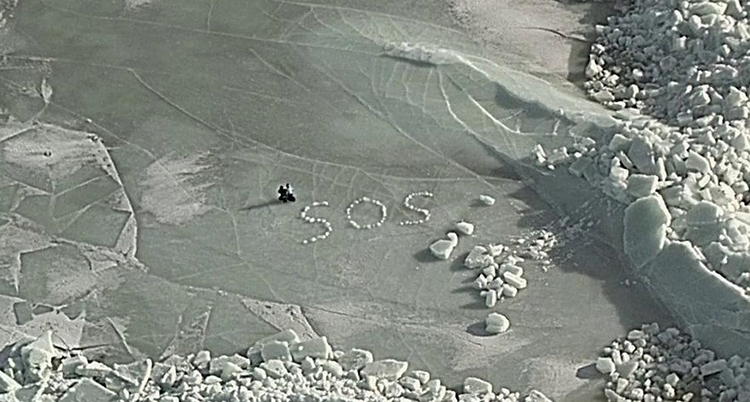 Männen är fast på isen på havet. Bredvid dem står det SOS med block av is.