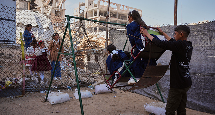 En pojke sätter fart på en gunga. Några barn sitter i gungan.