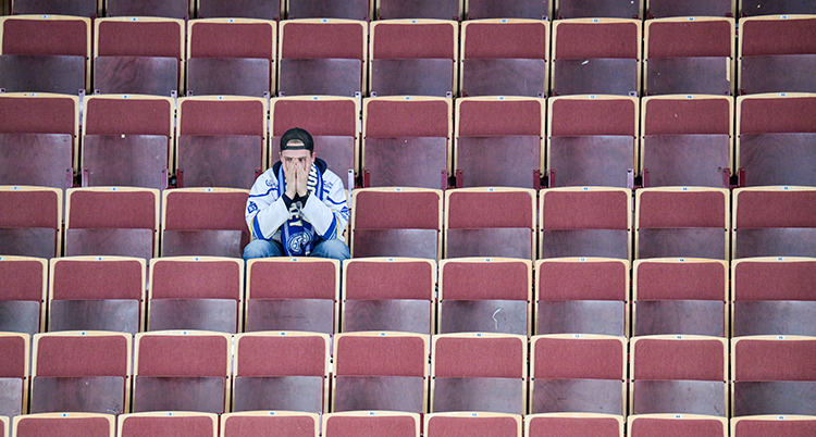 Han sitter ensam på en stol. Runt honom är det tomt på folk.