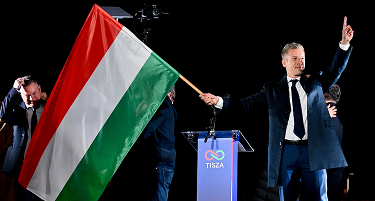 Han står på en scen och han har en stor flagga. Han är glad.