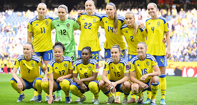 Sveriges damlandslag i fotboll står uppställda inför en match. Fem kvinnor sitter på huk. Sex kvinnor står bakom.