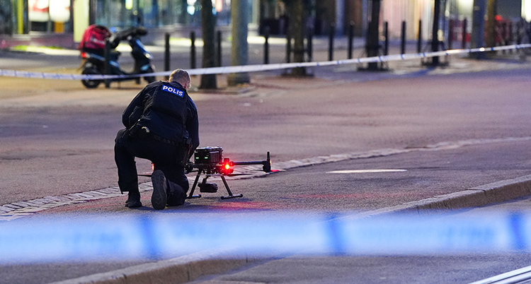 En polis sitter på knän på marken. Han jobbar med en drönare.