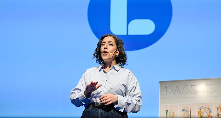 Hon står på en scen. Hon pratar. Hon har en liten mikrofon som sitter fast bakom örat.