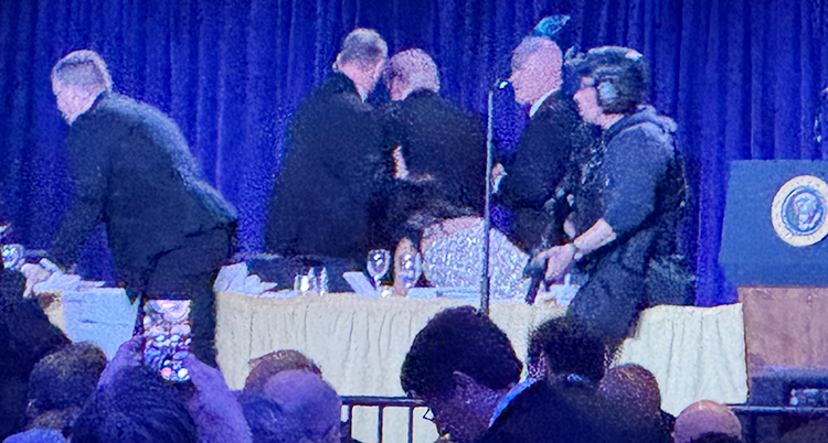 En stor middag. Donald Trump har suttit vid ett bord som är på en scen. Nu hjälper vakter honom att komma därifrån.