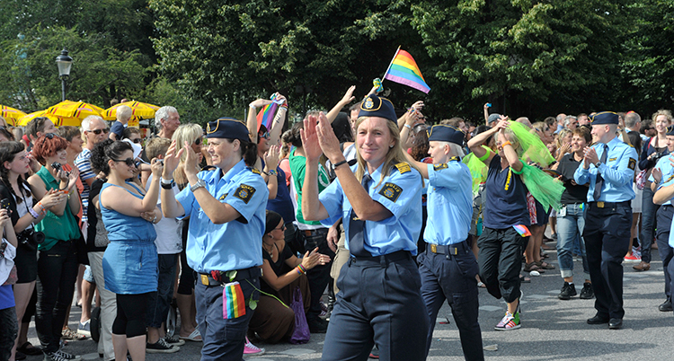 Poliser i uniform går i en klunga av människor. Flaggor med regnbågens färger syns.