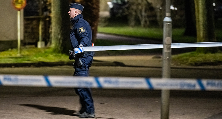 En polis står på en gata. Tejp som spärrar av platsen syns.