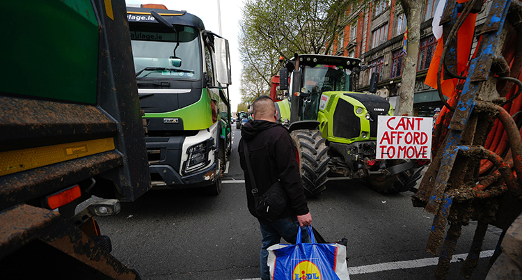 En man försöker gå över en gata där traktorer parkerat.