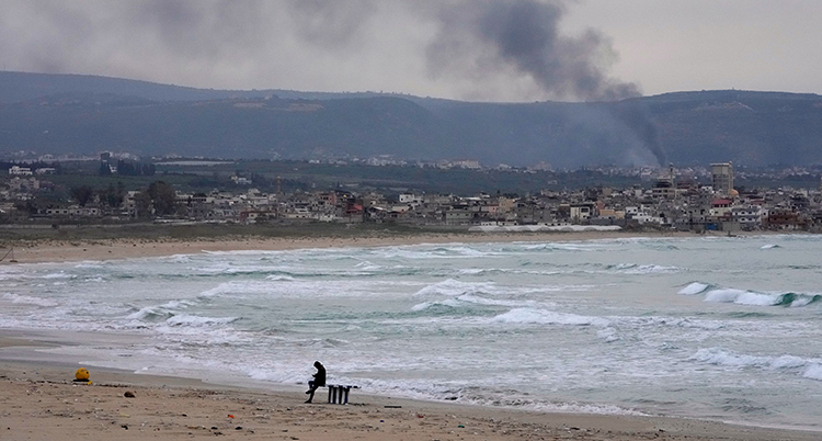 Havet och flera hus syns bakom mannen på stranden.