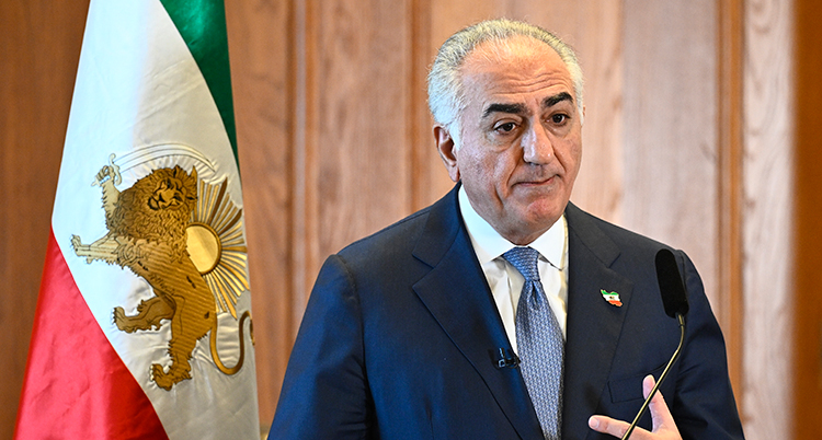 Han har slips och kostym. Han står framför en mikrofon.