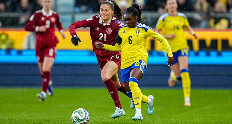 Hon springer vid sidan om en dansk spelare. De kämpar om bollen.