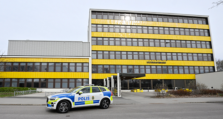 En skola som är gul och som har många fönster. En polisbil står utanför.