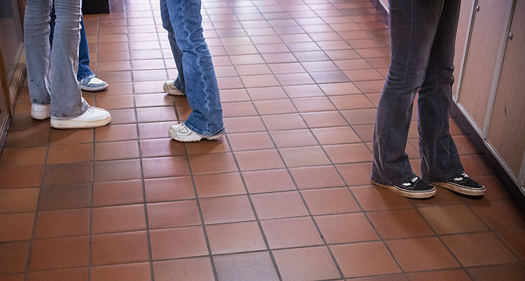 En korridor i en skola. Några elever står i korridoren. Bilden visar bara elevernas ben.
