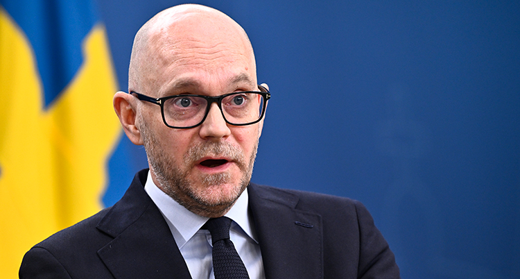 Han pratar på ett möte för journalister. En svensk flagga syns i bakgrunden.