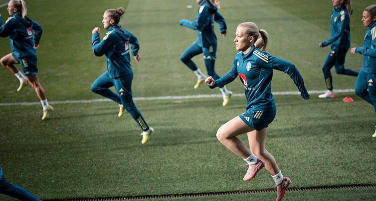 En fotbollsplan. Det är träning. Flera spelare springer med höga steg.