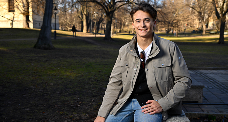 Han är utomhus. Han tittar in i kameran.