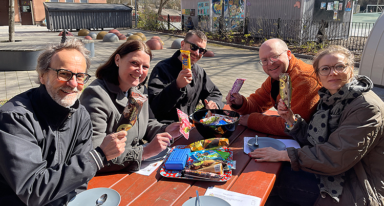 Fem personer håller i glassar och sitter ute vid ett bord.