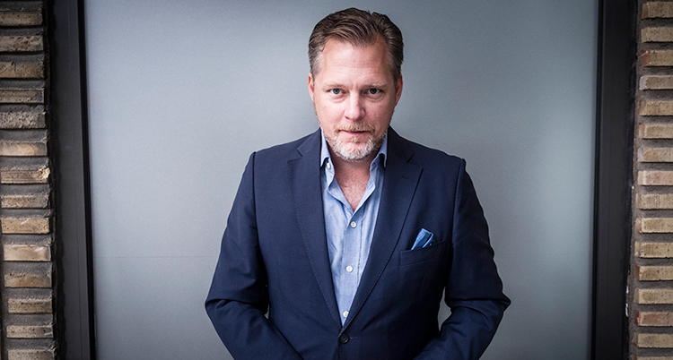 Han tittar in i kameran. Han har skjorta och kavaj.