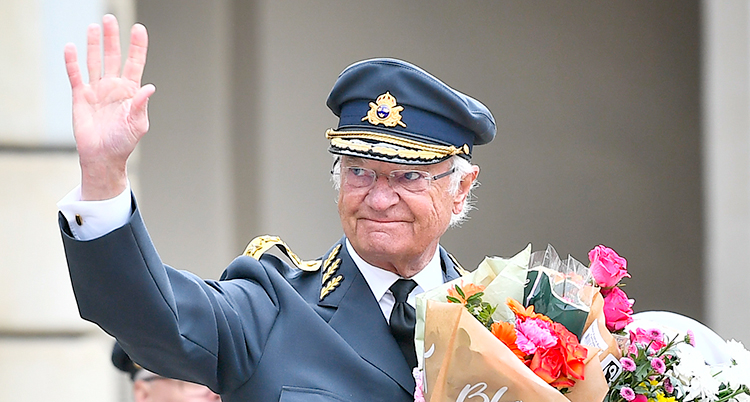 Kungen vinkar. Han håller i blommor.