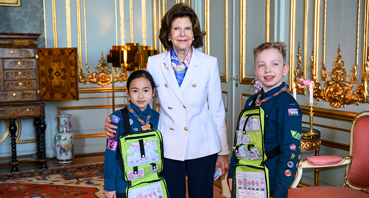 Barnen står bredvid drottningen. De har väskor med blommorna i.