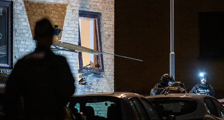 Det är mörkt ute. Poliser syns vid ett hus. Ett fönster är öppet och det syns skador på huset.