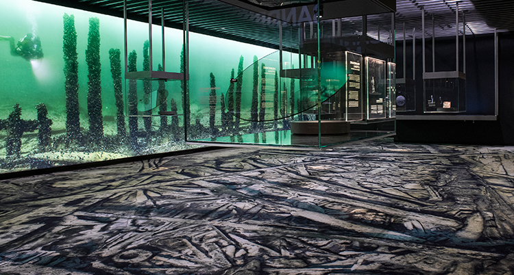 En monter med vatten och vrakdelar syns i bakgrunden av ett rum på museet.