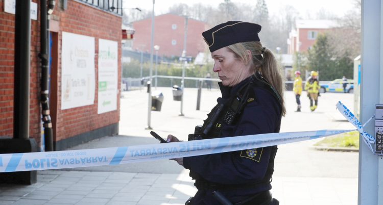 En kvinnlig polis står bakom polisernas band. Hon tittar i en mobil.