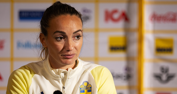 Hon sitter bakom en mikrofon. Hon har kläder för träning på sig.