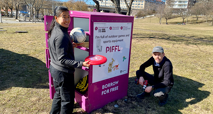 Hon håller i en boll och en frisbee. Han sitter på huk intill ett skåp med luckor.